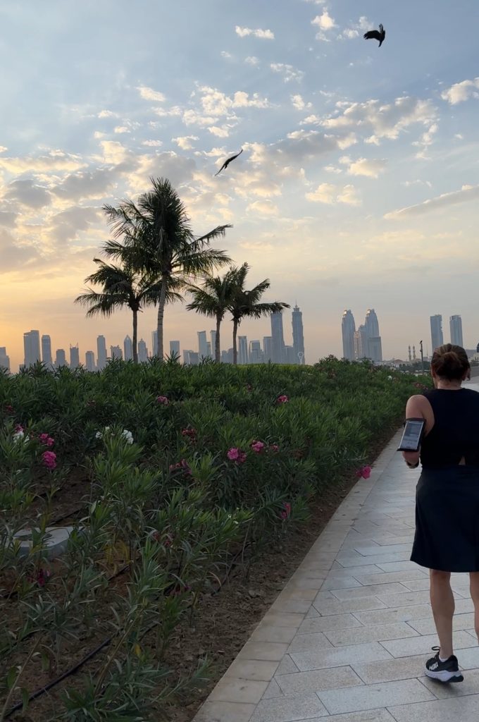 Femme sur chemin, palmiers et skyline au coucher du soleil.