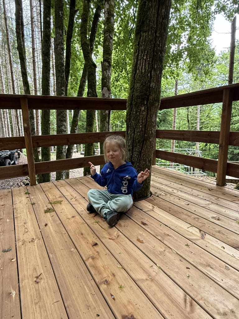 Enfant méditant sur terrasse en bois, forêt derrière.