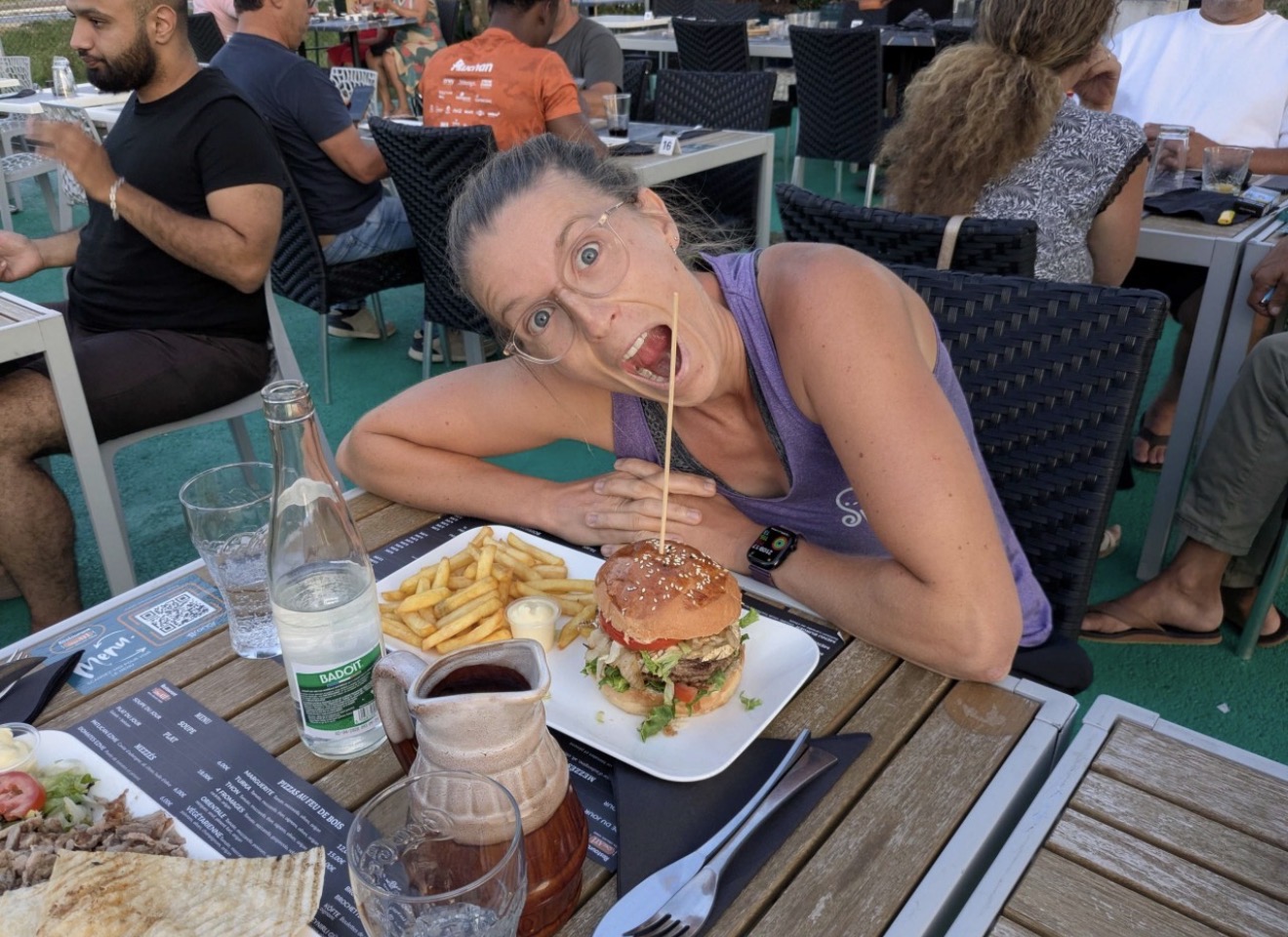 Femme souriante devant un hamburger et des frites en terrasse